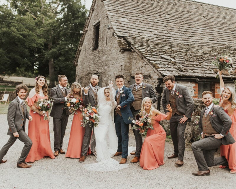 Bridesmaids and groomsmen in coral posing in front of the stone barns at Drovers Rest.