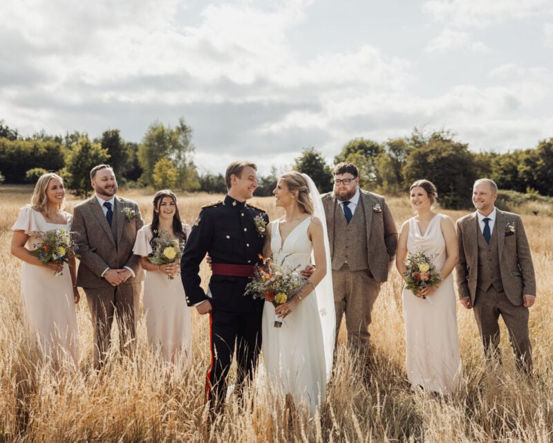 Bridesmaids and groomsmen posing in long grass at a wedding.